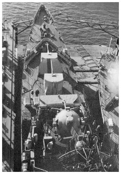 Blick aus dem Mast senkrecht auf das Vorschiff eines Küstenschutzschiffes im Werftdock mit abgedecktem 100-mm-Turm, Ankerspill und aufgestellten Leitern