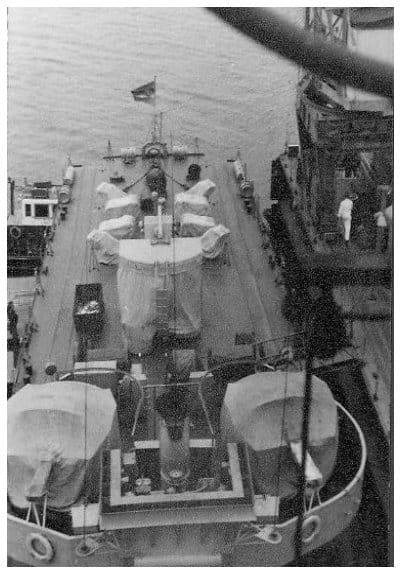 Blick aus dem Mast auf das Vorschiff eines Küstenschutzschiffes an der Werftpier mit abgedecktem Geschützturm, Wasserbombenwerfern und Rettungsinseln